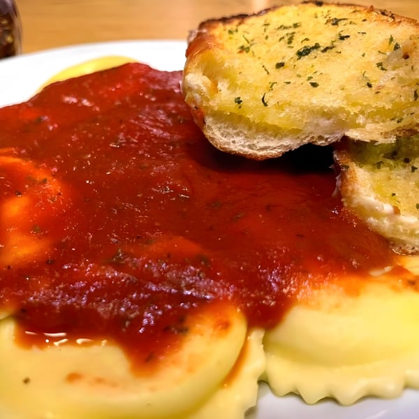 Close-up of ravioli covered in red sauce with two pieces of garlic bread on a white plate.