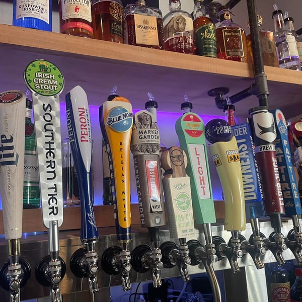 A close-up of multiple beer taps with various brand handles and liquor bottles on a shelf above.